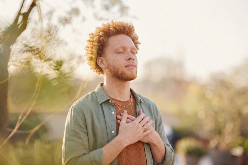 Un homme en extérieur les yeux fermés et les mains sur le cœur en pleine conscience, illustrant l'éveil spirituel