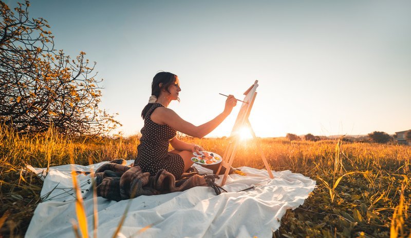 Femme assise dans la nature au crépuscule qui utilise son énergie féminine pour créer de l'art sur une toile.
